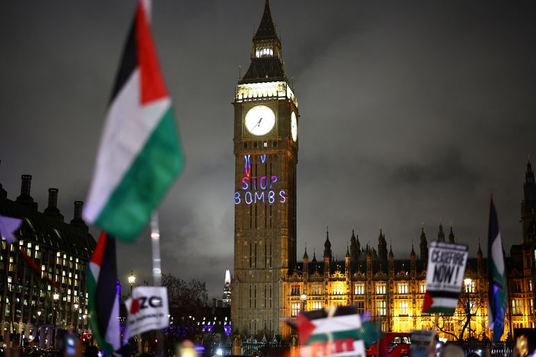 A Palestinian flag flaps in the air by a message reading "Stop bombs" projected on The Elizabeth Tower, commonly known by the name of the clock's bell "Big Ben", at the Palace of Westminster, home to the Houses of Parliament, during a Pro-Palestinian demonstration in Parliament Square in London on February 21, 2024, on the sidelines of the Opposition Day motion in the the House of Commons calling for an immediate ceasefire in Gaza. (Photo by HENRY NICHOLLS / AFP)