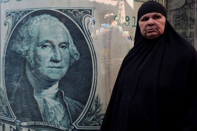 A woman stands next to a currency exchange point, displaying an image of the U.S. dollar, in Cairo, Egypt