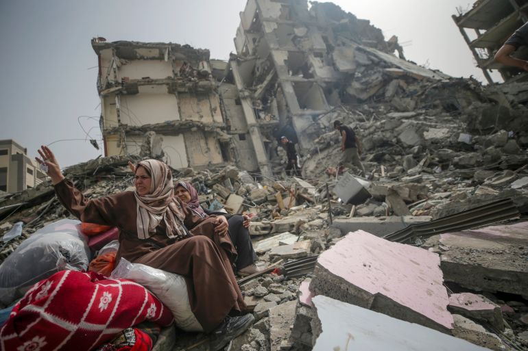 Palestinian women sit among the rubble of a house after returning to Al Nusairat refugee camp